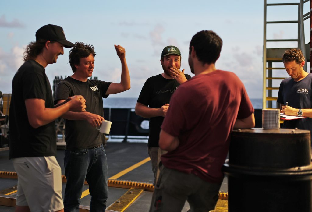 Members of the Alvin operations team enjoy early-morning coffee and conversation on the aft deck on August 18, 2022. In total, the whole team consumed 140 pounds of coffee. Photo by Marley Parker © Woods Hole Oceanographic Institution